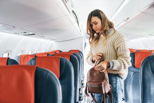 With lugagge. Young female passanger in casual clothes is in the plane.