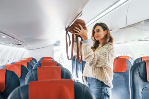 Holding lugagge. Young female passanger in casual clothes is in the plane.