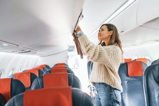 Holding lugagge. Young female passanger in casual clothes is in the plane.