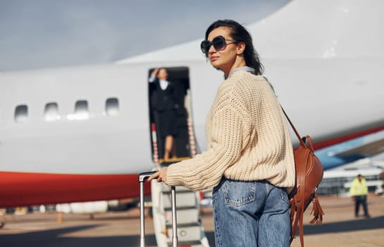 At daytime. Young female passanger in casual clothes is outdoors near the plane.