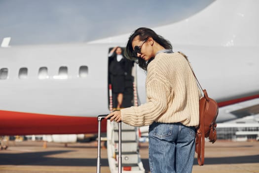 At daytime. Young female passanger in casual clothes is outdoors near the plane.