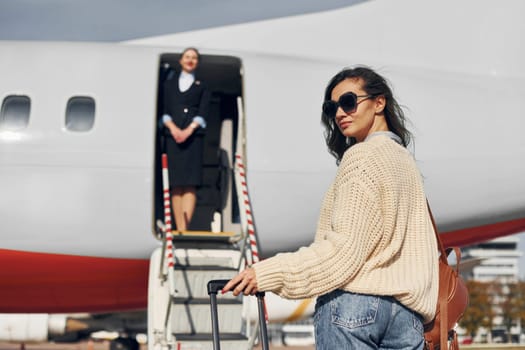 Young female passanger in casual clothes is outdoors near the plane.