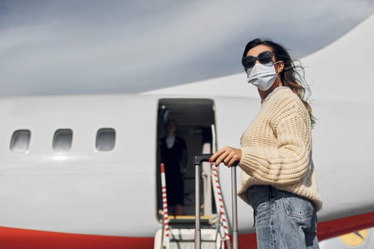 Young female passanger in casual clothes is outdoors near the plane.