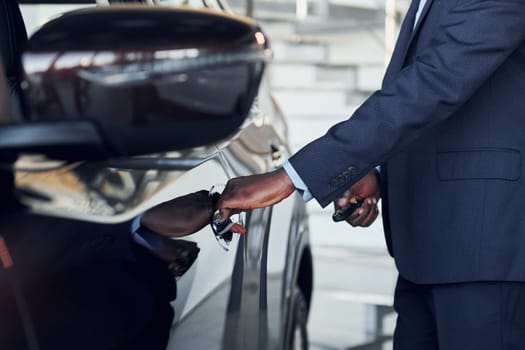 Opening the door. Young african american businessman in black suit is the autosalon.