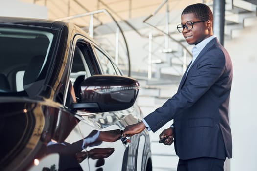Opening the door. Young african american businessman in black suit is the autosalon.