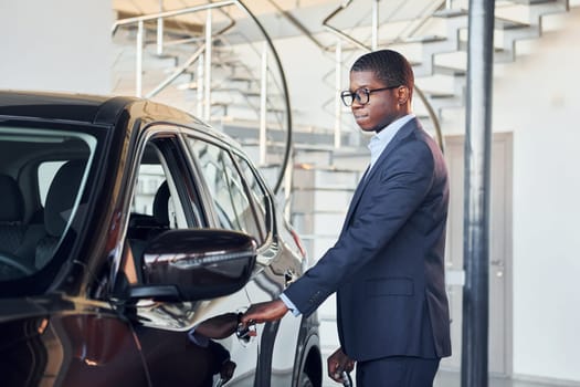 Opening the door. Young african american businessman in black suit is the autosalon.