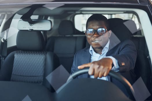 Positive mood. Young african american businessman in black suit is in the automobile.