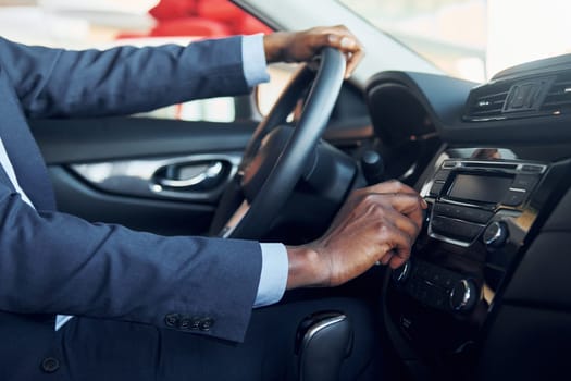 Side view. Young african american businessman in black suit is in the automobile.