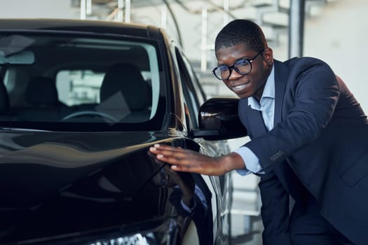 Young african american businessman in black suit is the autosalon.