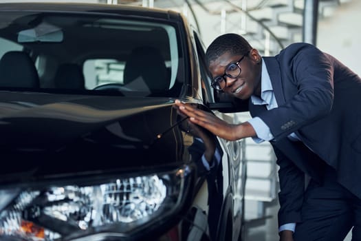 Young african american businessman in black suit is the autosalon.
