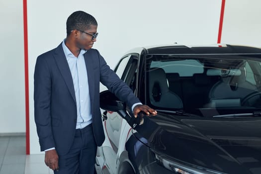 Young african american businessman in black suit is the autosalon.