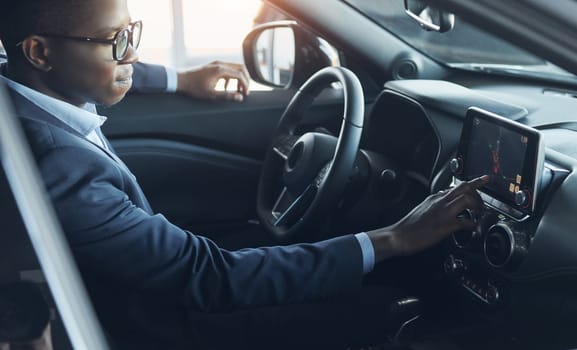 Using front control panel. Young african american businessman in black suit is in the automobile.
