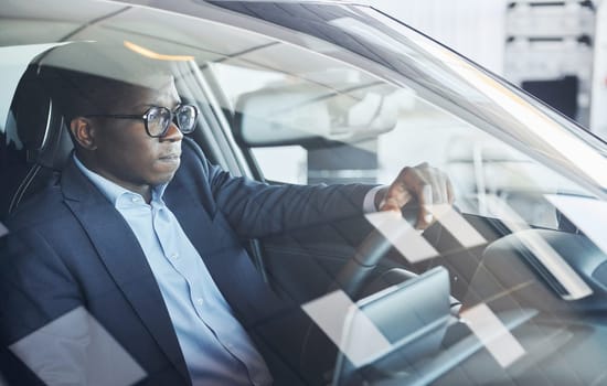 Vehicle interior. Young african american businessman in black suit is in the automobile.