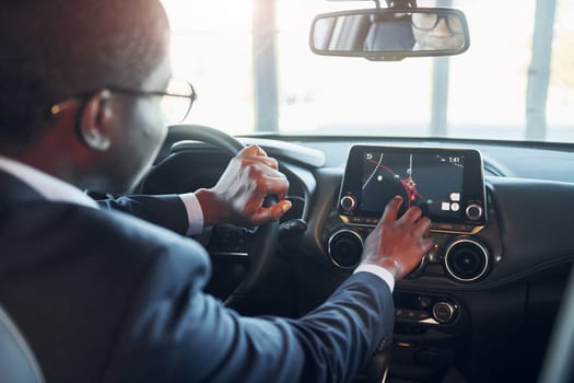 Vehicle interior. Young african american businessman in black suit is in the automobile.
