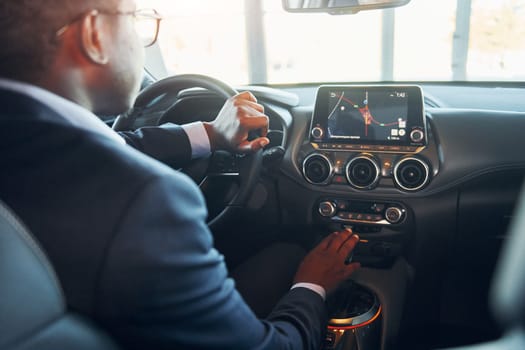 Rear view. Young african american businessman in black suit is in the automobile.