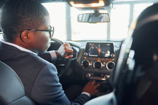 Rear view. Young african american businessman in black suit is in the automobile.