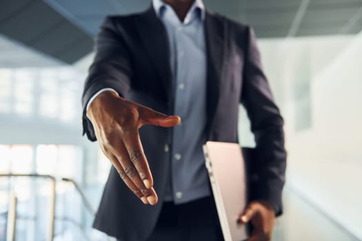 Handshake gesture. Young african american businessman in black suit is indoors.