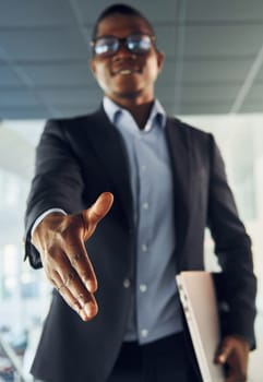 Handshake gesture. Young african american businessman in black suit is indoors.