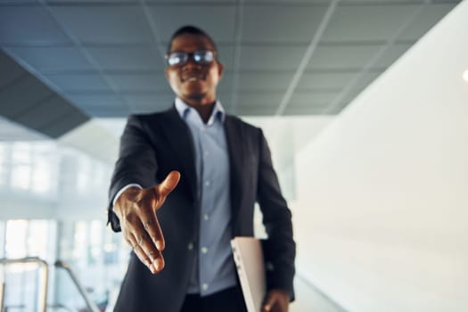 Handshake gesture. Young african american businessman in black suit is indoors.