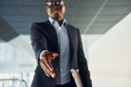 Handshake gesture. Young african american businessman in black suit is indoors.