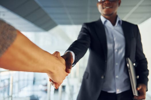 Successfull agreement. Young african american businessman in black suit is indoors.