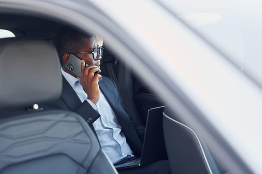 Passanger on the back seat. Young african american businessman in black suit is in the automobile.