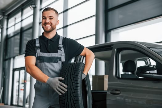 Brand new tire. Man in uniform is working in the autosalon at daytime.