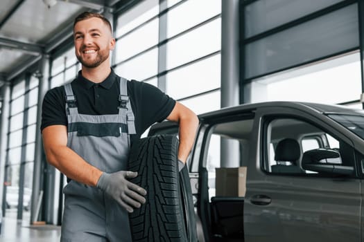 Brand new tire. Man in uniform is working in the autosalon at daytime.