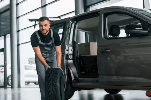 Brand new tire. Man in uniform is working in the autosalon at daytime.