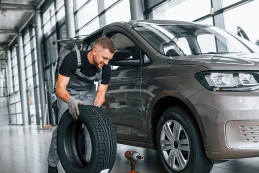 Time to change tires. Man in uniform is working in the autosalon at daytime.