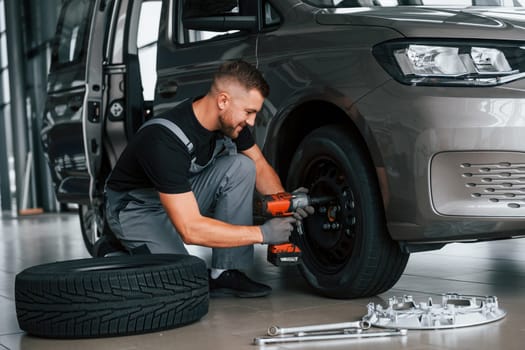 Time to change tires. Man in uniform is working in the autosalon at daytime.