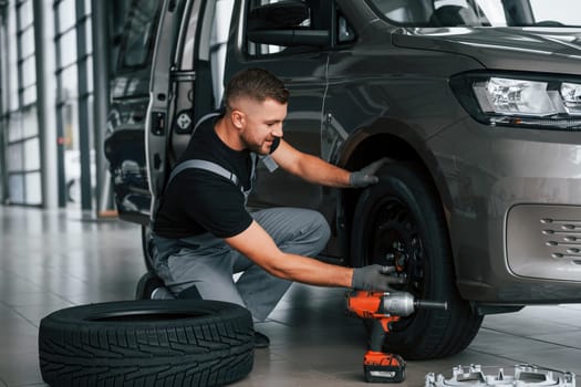 Time to change tires. Man in uniform is working in the autosalon at daytime.