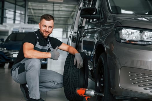 Changing of the tires. Man in uniform is working in the autosalon at daytime.