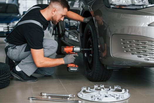 Changing of the tires. Man in uniform is working in the autosalon at daytime.