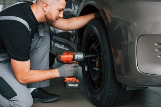 Changing of the tires. Man in uniform is working in the autosalon at daytime.