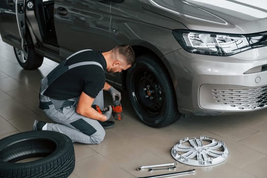 Changing of the tires. Man in uniform is working in the autosalon at daytime.