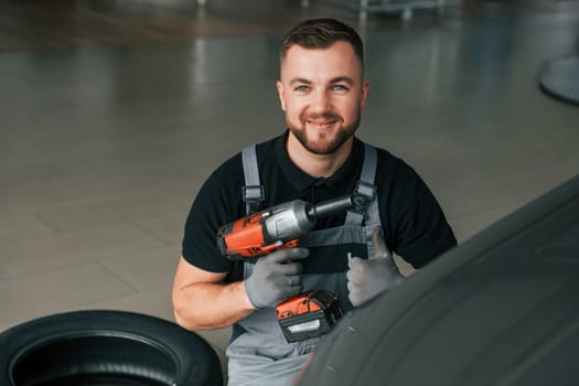 Using equipment. Man in uniform is working in the autosalon at daytime.