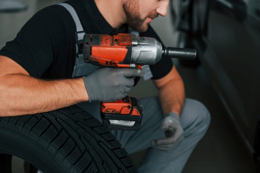 Using equipment. Man in uniform is working in the autosalon at daytime.