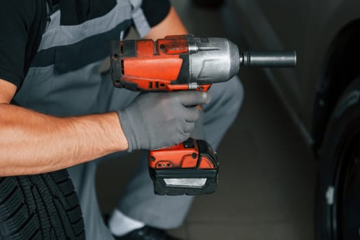 Using equipment. Man in uniform is working in the autosalon at daytime.