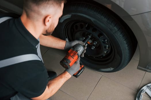 Using equipment. Man in uniform is working in the autosalon at daytime.