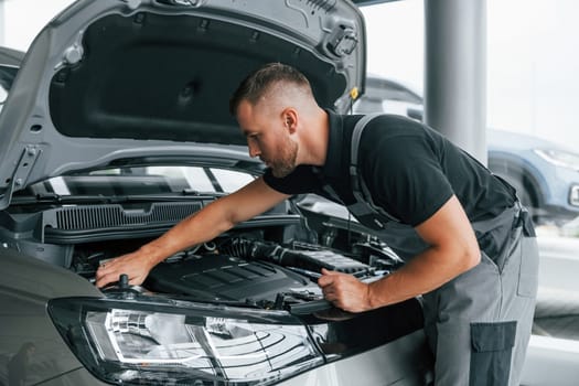 Under the hood. Man in uniform is working in the autosalon at daytime.