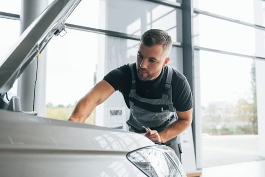 Repairing of the car. Man in uniform is working in the autosalon at daytime.