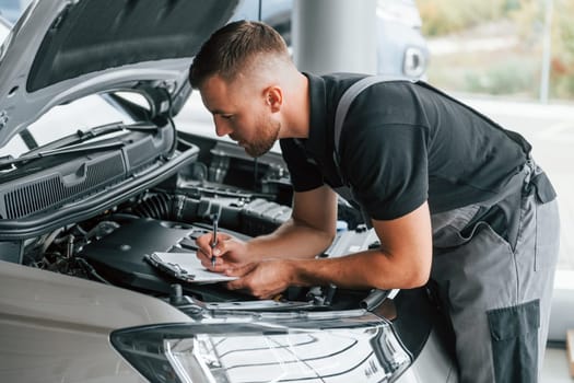 Repairing of the car. Man in uniform is working in the autosalon at daytime.