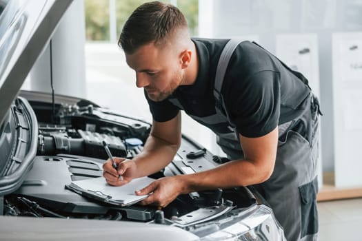 Repairing of the car. Man in uniform is working in the autosalon at daytime.