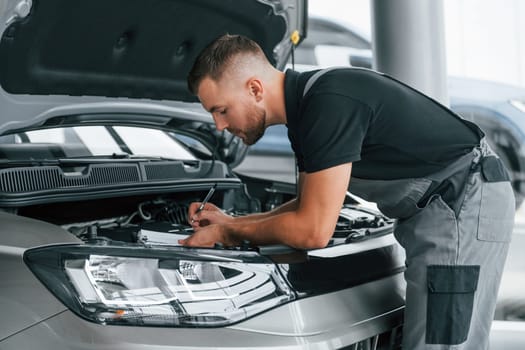 Repairing of the car. Man in uniform is working in the autosalon at daytime.
