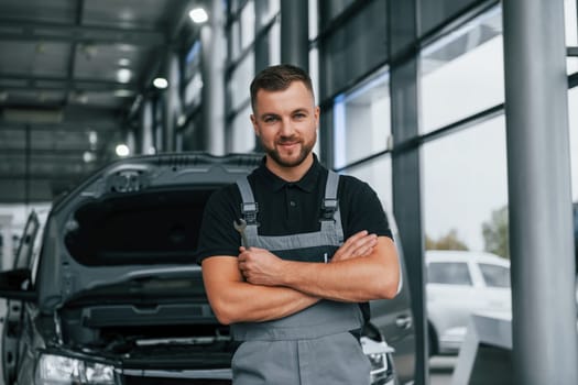 Arms crossed. Man in uniform is working in the autosalon at daytime.