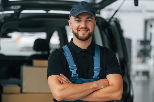 Positive emotions. Delivery man in uniform is indoors with car and with order.