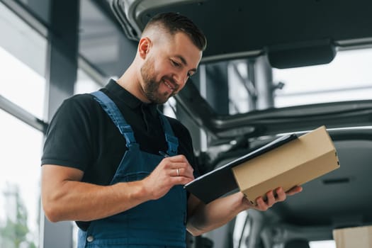 Positive emotions. Delivery man in uniform is indoors with car and with order.