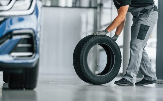 Tire on the floor. Man in uniform is working in the autosalon at daytime.