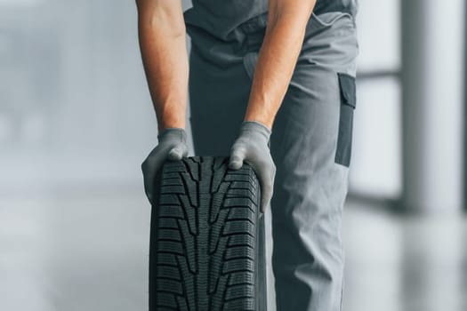 Tire on the floor. Man in uniform is working in the autosalon at daytime.